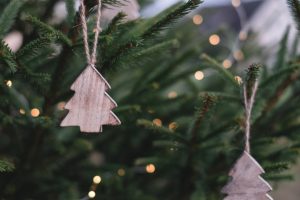 Close up photo of wooden tree ornaments on evergreen tree with white lights